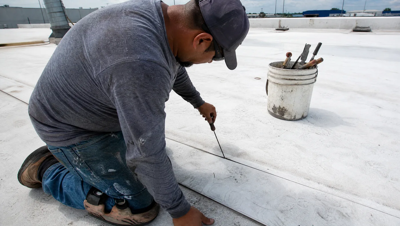 Roofer probing a failed seam on a Houston commercial TPO roof